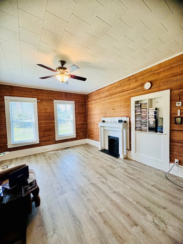 unfurnished living room with wood walls, ceiling fan, and light hardwood / wood-style floors