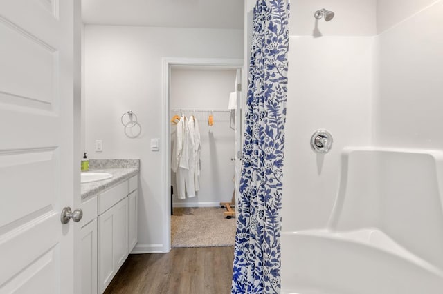 bathroom featuring curtained shower, a spacious closet, vanity, wood finished floors, and baseboards