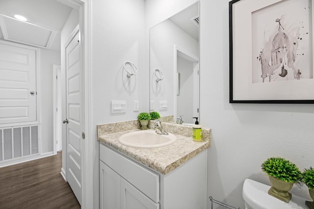 half bathroom with toilet, visible vents, wood finished floors, and vanity