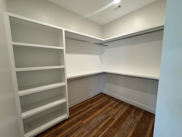 spacious closet with built in desk, visible vents, and dark wood-type flooring