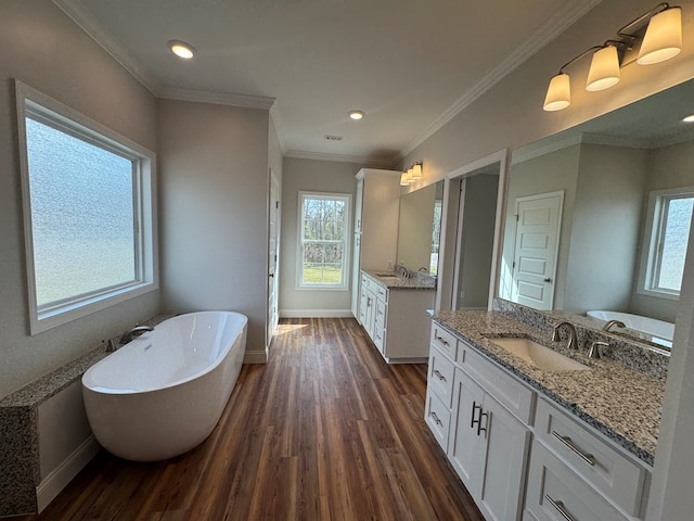 bathroom featuring wood finished floors, a sink, baseboards, a soaking tub, and crown molding