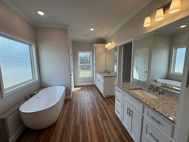 bathroom featuring baseboards, wood finished floors, crown molding, a freestanding bath, and a sink