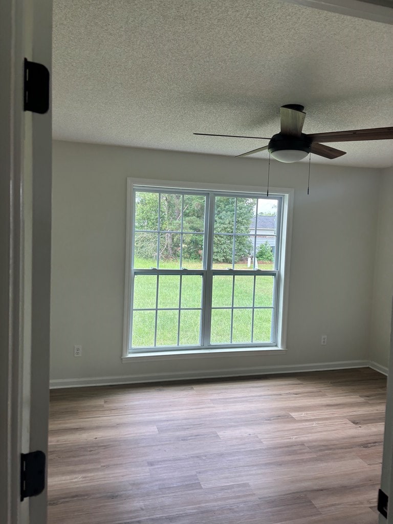 1000 E Gate Dr, Bainbridge, GA 39817 - unfurnished room featuring a textured ceiling, a ceiling fan, plenty of natural light, and wood finished floors