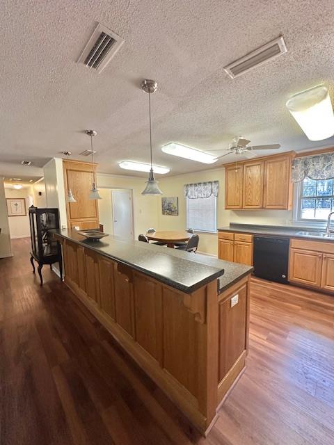 kitchen featuring hanging light fixtures, hardwood / wood-style flooring, black dishwasher, and sink