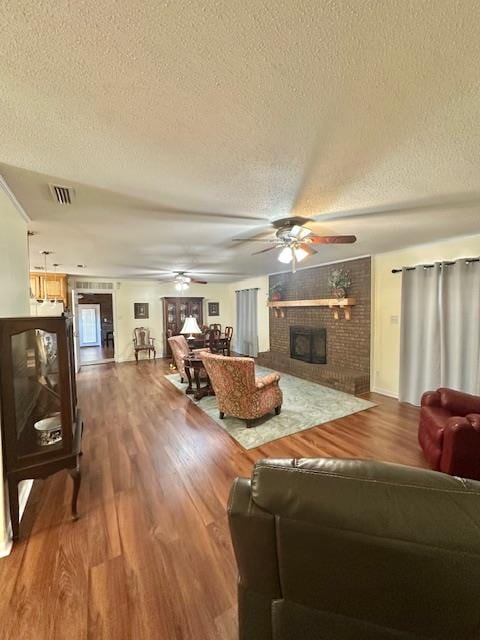 living room featuring ceiling fan, hardwood / wood-style floors, a fireplace, and a textured ceiling