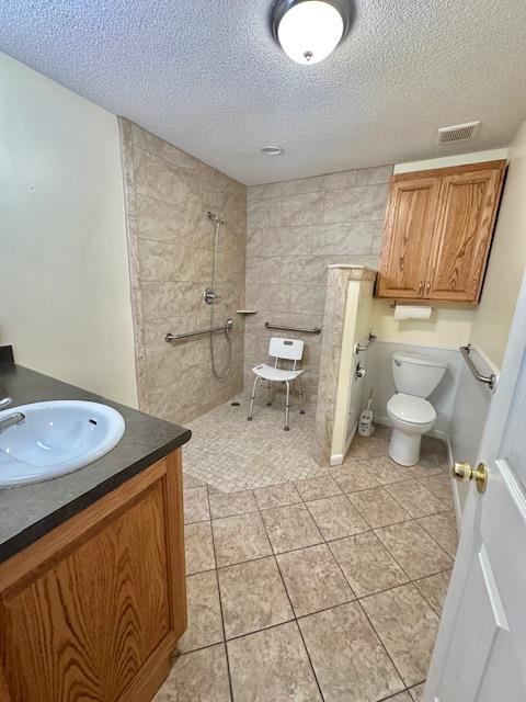 bathroom with tile patterned flooring, tiled shower, vanity, a textured ceiling, and toilet