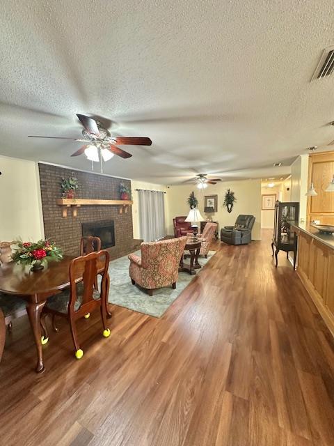 dining space featuring hardwood / wood-style flooring, ceiling fan, a brick fireplace, and a textured ceiling