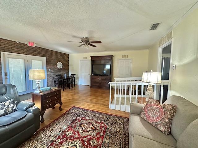 living room with hardwood / wood-style flooring, ceiling fan, brick wall, and a textured ceiling