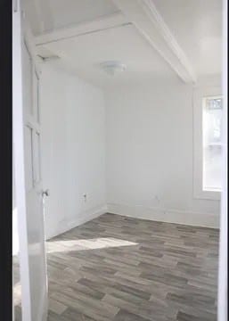 spare room featuring beamed ceiling and dark hardwood / wood-style flooring