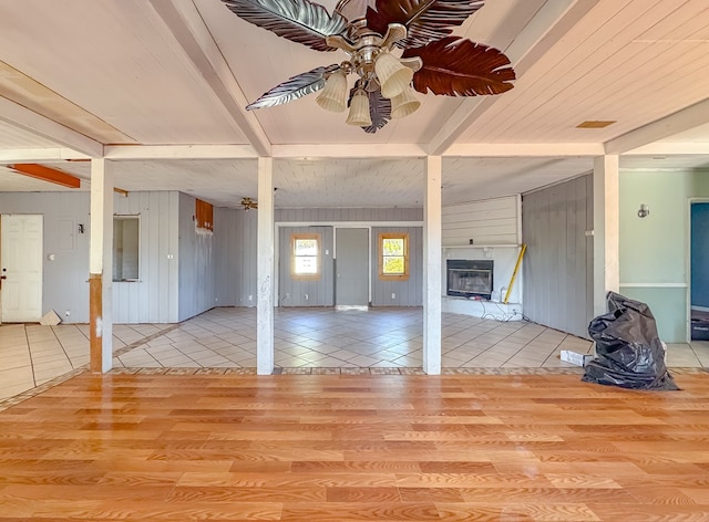 unfurnished living room with ceiling fan, light wood-type flooring, wood walls, and beamed ceiling