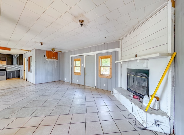 unfurnished living room with ceiling fan, wooden walls, and light tile patterned flooring