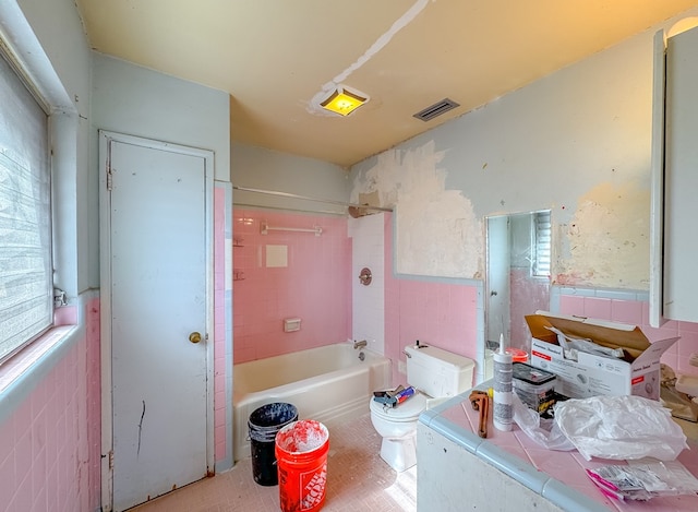 bathroom with toilet, tile walls, and tiled shower / bath