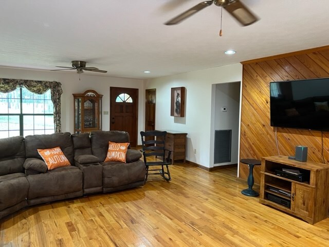 living room featuring wood walls, light hardwood / wood-style flooring, and ceiling fan