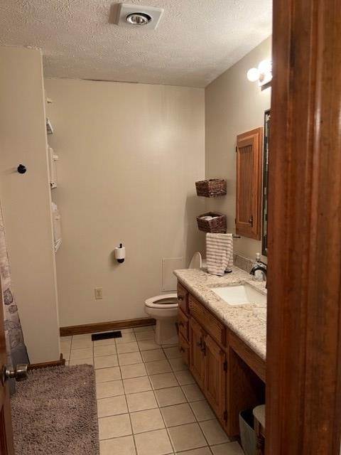 bathroom with tile patterned flooring, vanity, a textured ceiling, and toilet