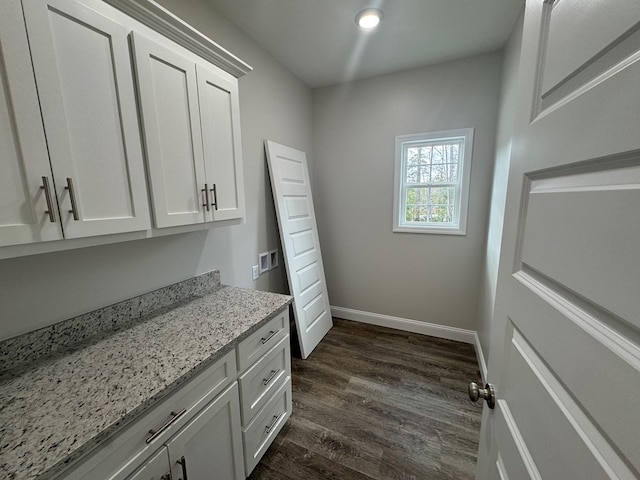 clothes washing area with cabinet space, dark wood finished floors, and baseboards