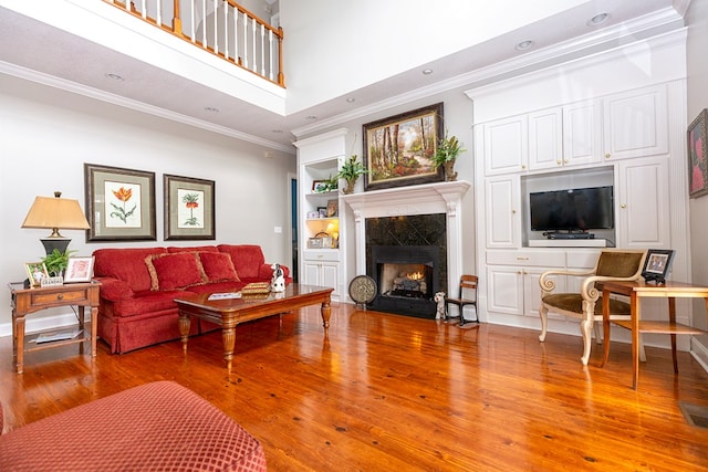 living room with wood-type flooring, ornamental molding, and a high end fireplace