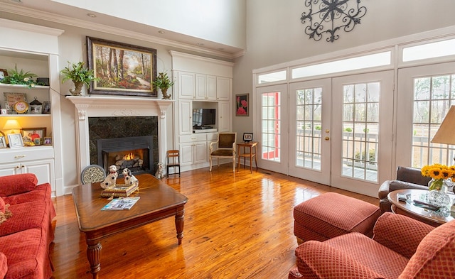 living room with french doors, a premium fireplace, a towering ceiling, ornamental molding, and light hardwood / wood-style floors