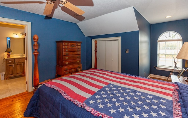 bedroom featuring lofted ceiling, ensuite bath, ceiling fan, wood-type flooring, and a closet