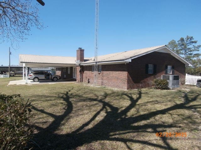 back of house featuring brick siding, a lawn, central AC unit, fence, and an attached carport