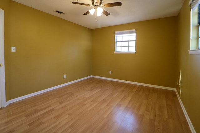 empty room featuring a ceiling fan, light wood-style flooring, baseboards, and visible vents