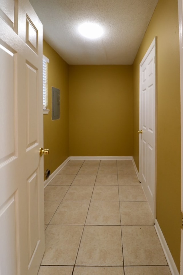 corridor featuring electric panel, light tile patterned floors, a textured ceiling, and baseboards