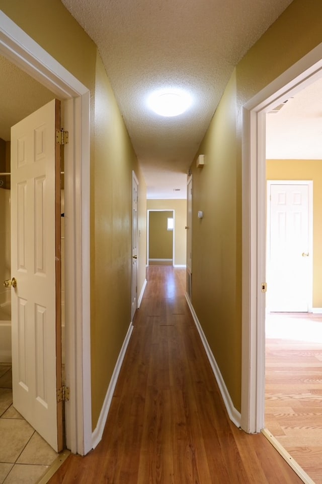 hallway with wood finished floors, baseboards, and a textured ceiling