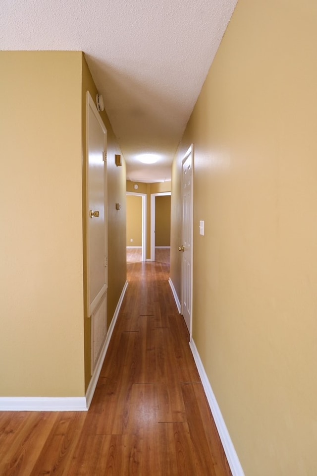 hall featuring a textured ceiling, baseboards, and wood finished floors