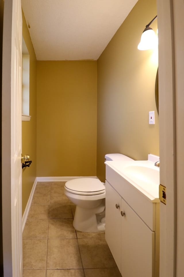 half bath with tile patterned flooring, toilet, vanity, and baseboards