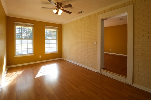 spare room with visible vents, brick wall, ornamental molding, wood finished floors, and a textured ceiling