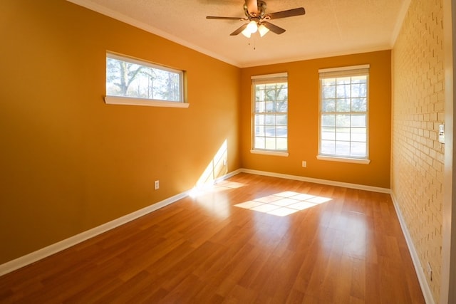 spare room with ornamental molding, a ceiling fan, wood finished floors, brick wall, and baseboards