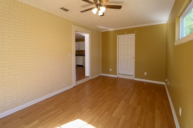 unfurnished room featuring wood finished floors, visible vents, brick wall, and baseboards