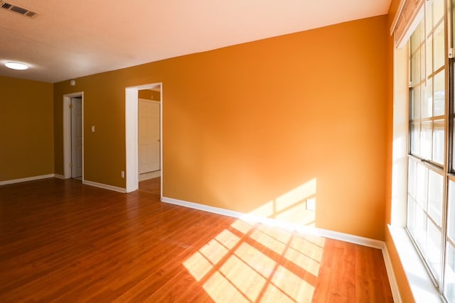 unfurnished room featuring wood finished floors, visible vents, and baseboards