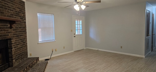 unfurnished living room featuring a textured ceiling, wood finished floors, baseboards, a brick fireplace, and ceiling fan