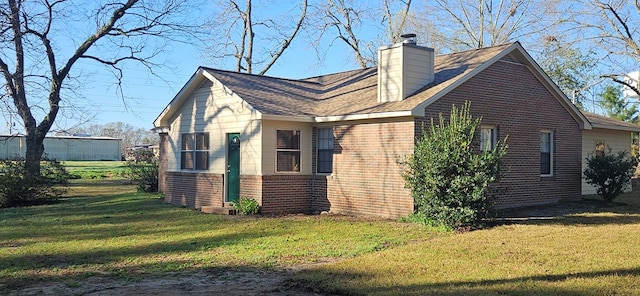 view of side of property with a yard, brick siding, roof with shingles, and a chimney