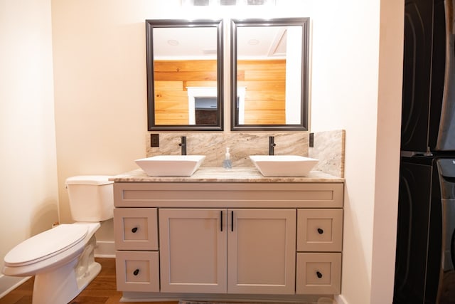 bathroom featuring wood-type flooring, toilet, decorative backsplash, vanity, and stacked washer and clothes dryer