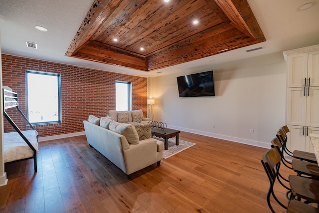 living room featuring a raised ceiling, wood ceiling, brick wall, and light wood-type flooring