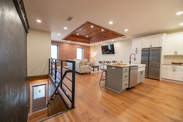 kitchen featuring a raised ceiling, a kitchen island with sink, white cabinets, and stainless steel appliances