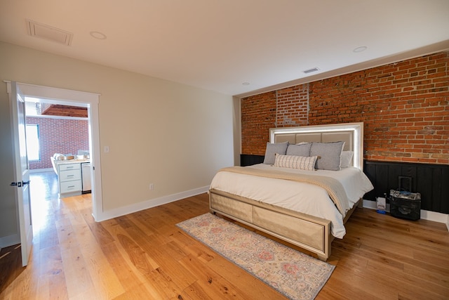 bedroom with light wood-type flooring and brick wall