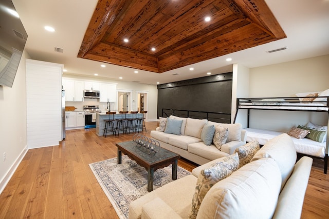 living room with light wood-type flooring, a tray ceiling, and sink