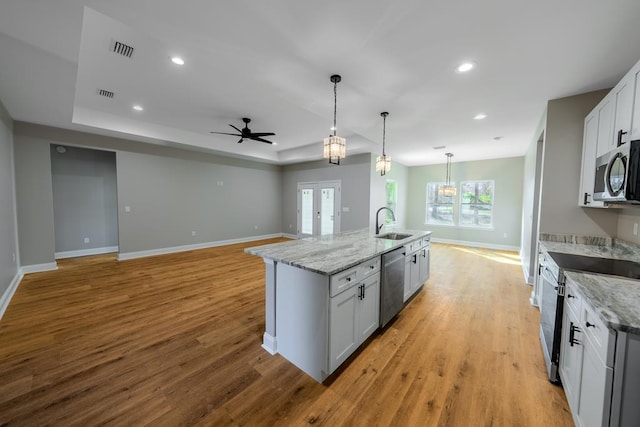 kitchen with stainless steel appliances, a sink, visible vents, light wood-style floors, and an island with sink