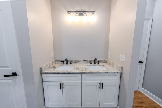 bathroom with double vanity, wood finished floors, a sink, and baseboards