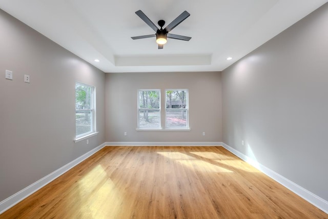 unfurnished room with ceiling fan, recessed lighting, light wood-style floors, baseboards, and a tray ceiling