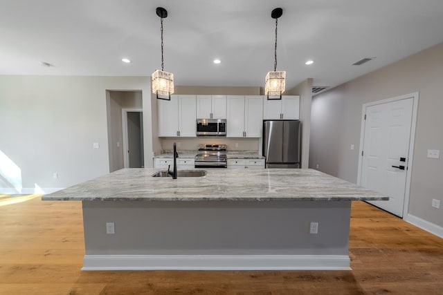 kitchen featuring appliances with stainless steel finishes, white cabinets, a sink, light wood-type flooring, and a large island with sink