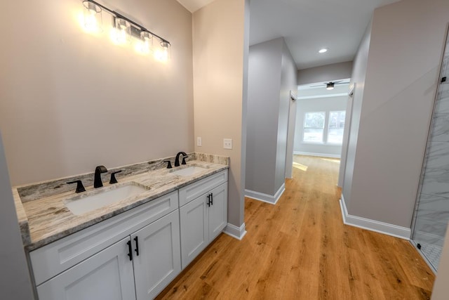 bathroom featuring double vanity, wood finished floors, a sink, and baseboards