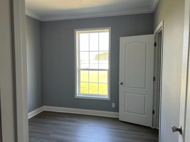 empty room with baseboards, dark wood finished floors, and crown molding