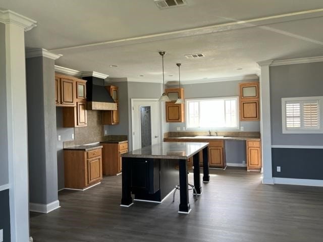 kitchen featuring premium range hood, baseboards, dark wood-style floors, brown cabinetry, and crown molding