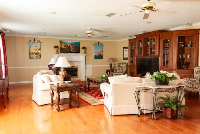 living area with light wood finished floors, a premium fireplace, ceiling fan, ornamental molding, and a textured ceiling