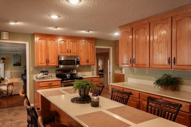 kitchen featuring a textured ceiling, light countertops, a breakfast bar area, and stainless steel appliances