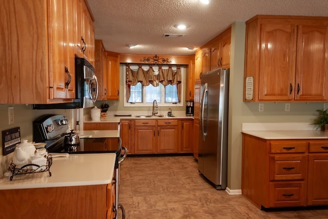 kitchen featuring brown cabinetry, stainless steel appliances, light countertops, and a sink