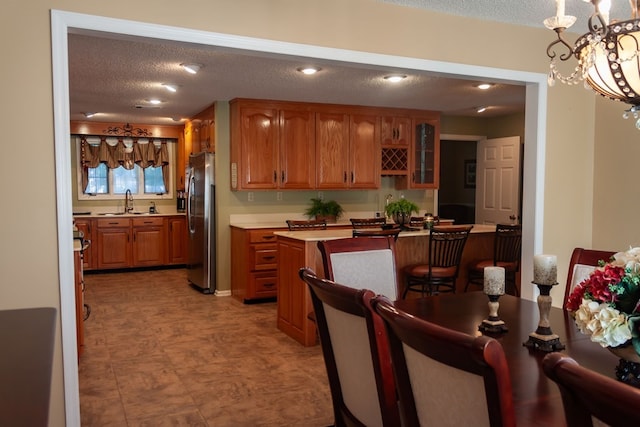 kitchen featuring brown cabinets, a textured ceiling, freestanding refrigerator, light countertops, and glass insert cabinets